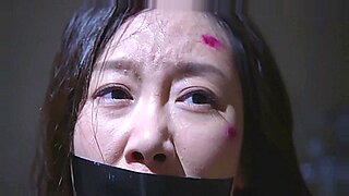 Une beauté asiatique tapote sa bouche, étouffant sur une grosse bite dans une scène BDSM.