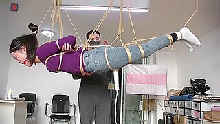 Una chica asiática colgando soporta restricciones BDSM y provocación.